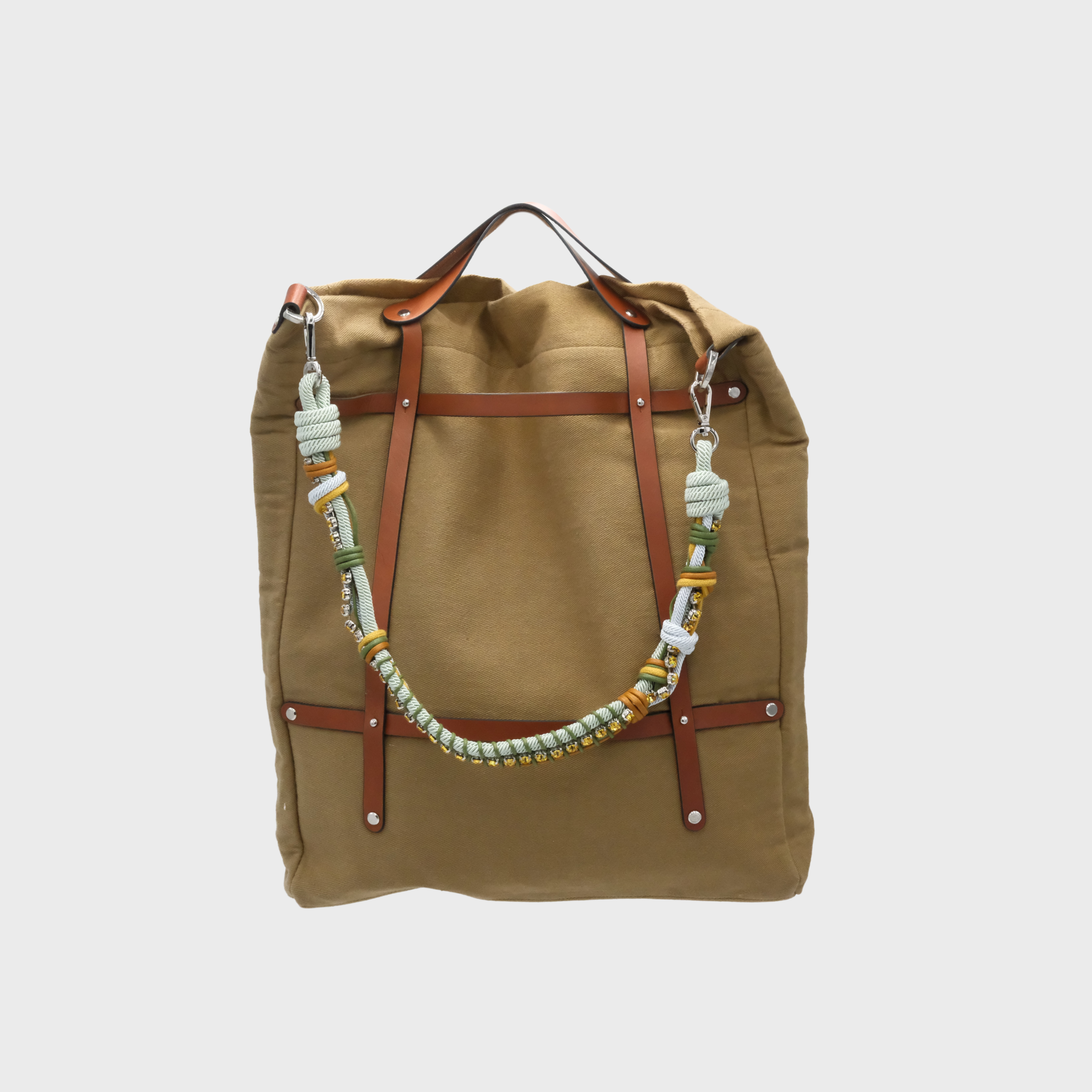 A canvas tote bag in a Taupe color, featuring brown leather straps and a decorative beaded shoulder strap with green, white, and gold details.