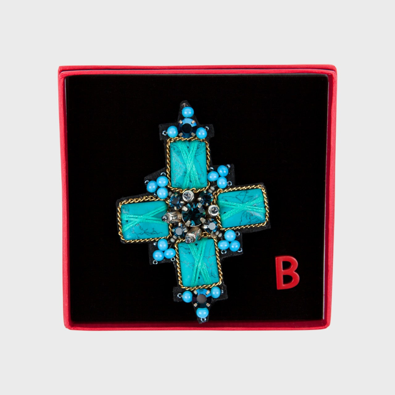 An embroidered brooch representing a blue cross in a box.