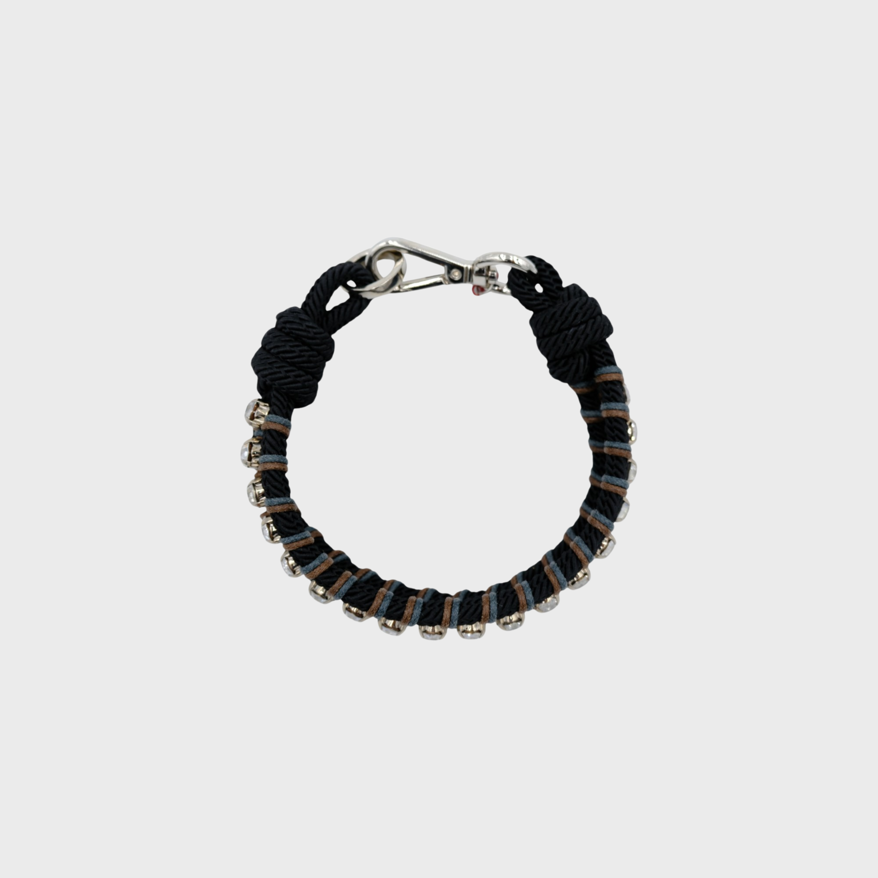 A photo taken from above of a braided macramé collar featuring black, blue and brown cords with small diamond beads and a silver clasp.