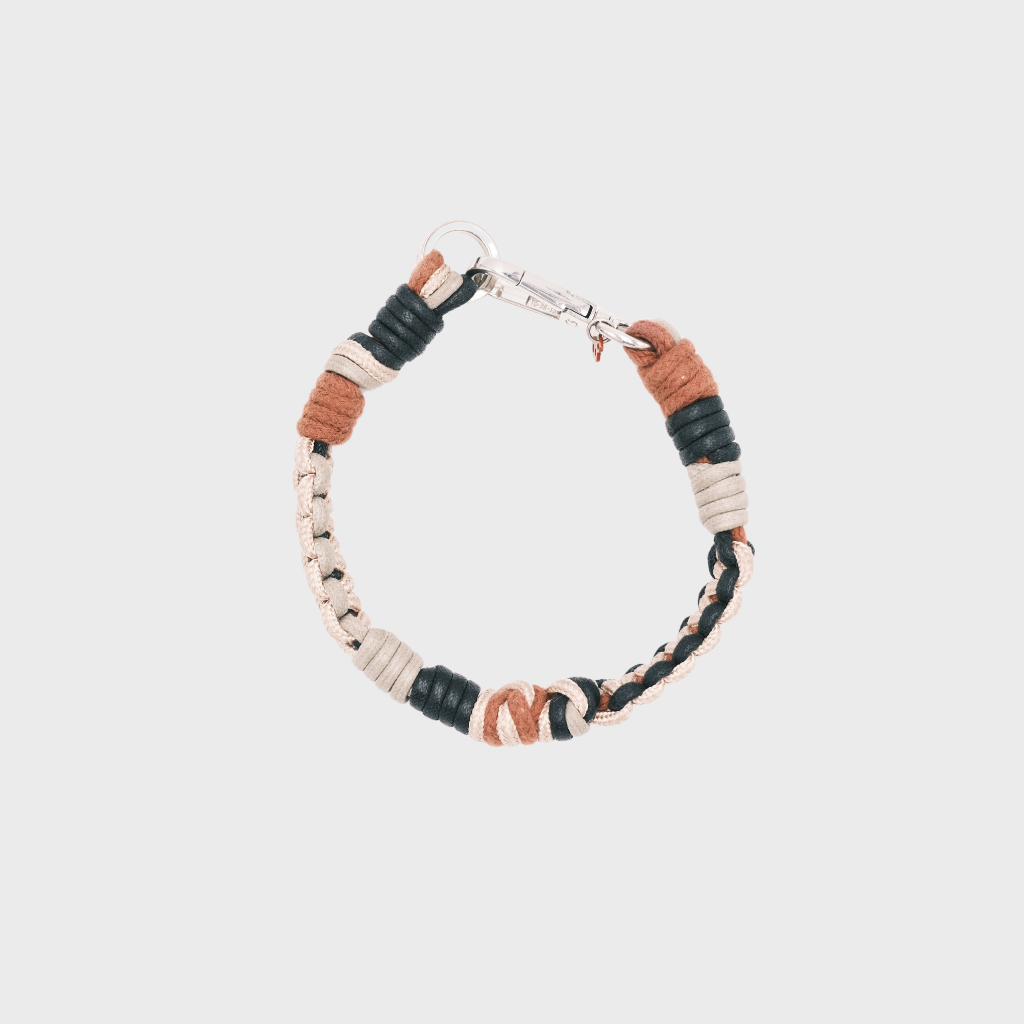 Photo taken from above of a handmade braided macramé cord collar in white, beige, black and brown with a silver clasp.
