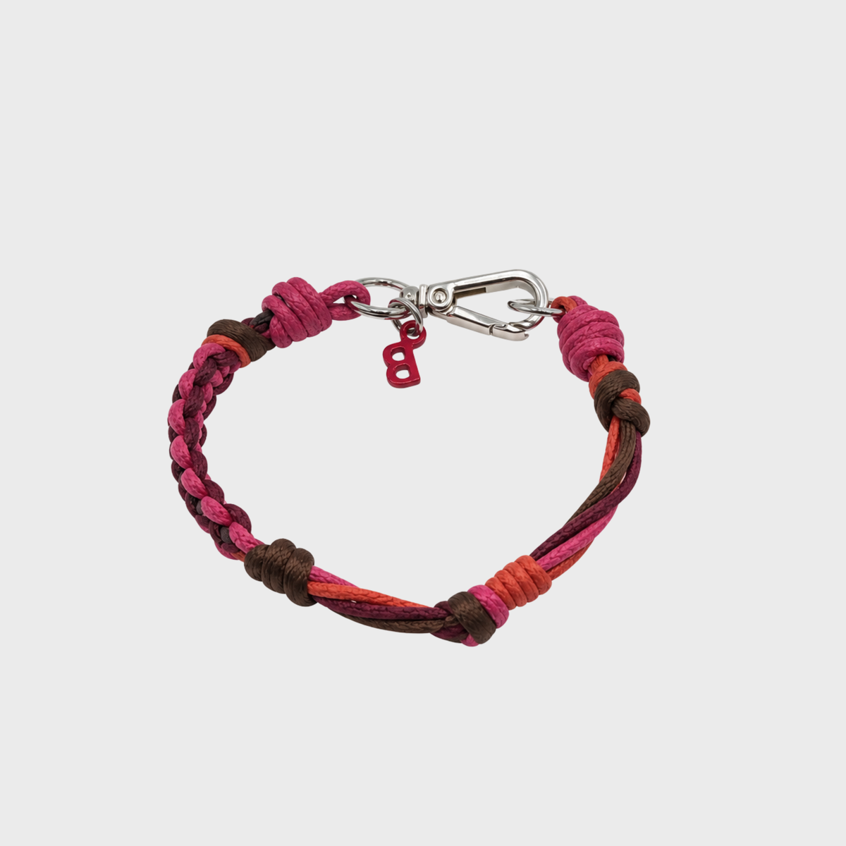 A braided cord bracelet in shades of pink, brown, and orange, featuring a silver-tone metal lobster clasp and a small red 'B' charm, shown against a light gray background.