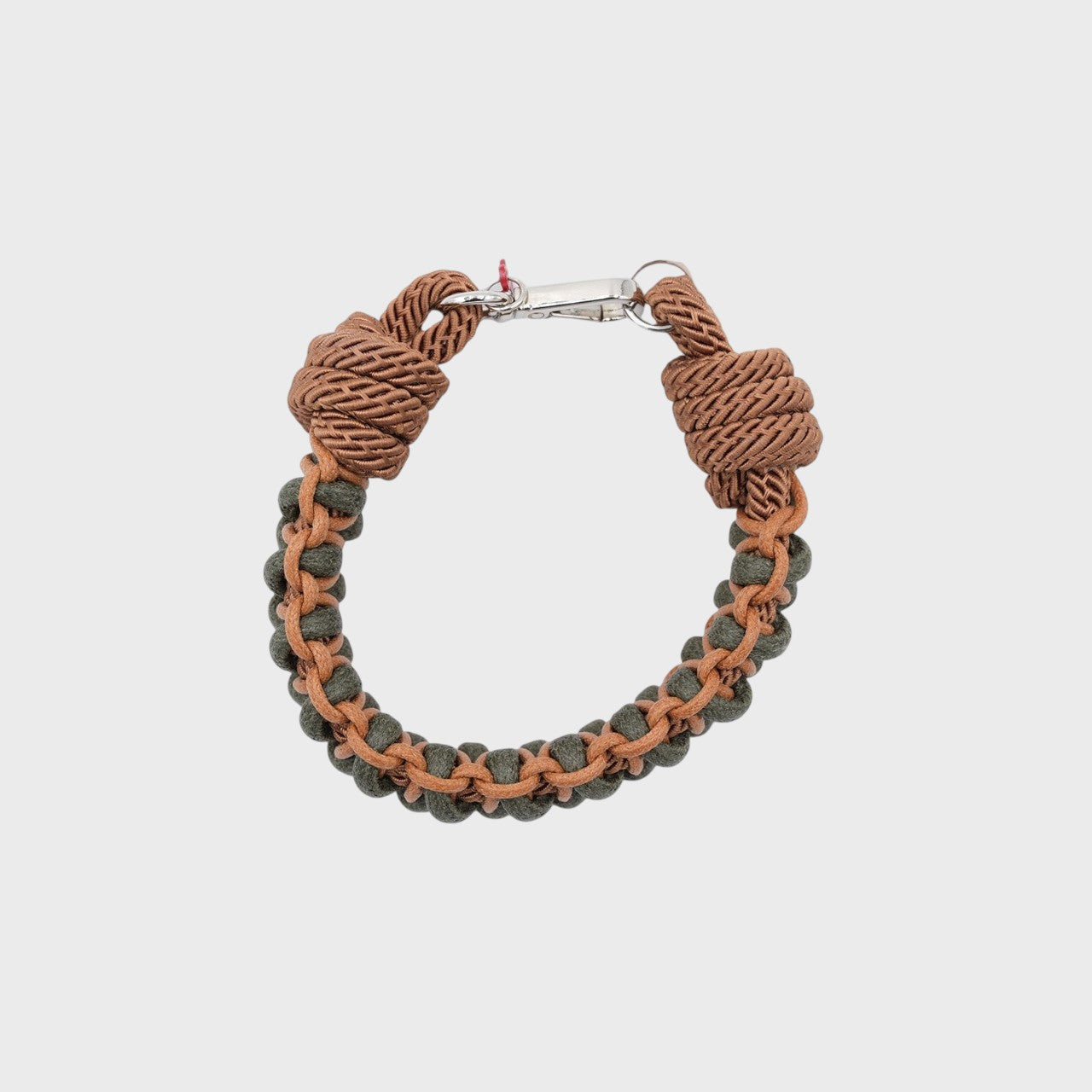 A photo taken from above of a braided macramé bracelet in shades of brown and dark green with a silver clasp.