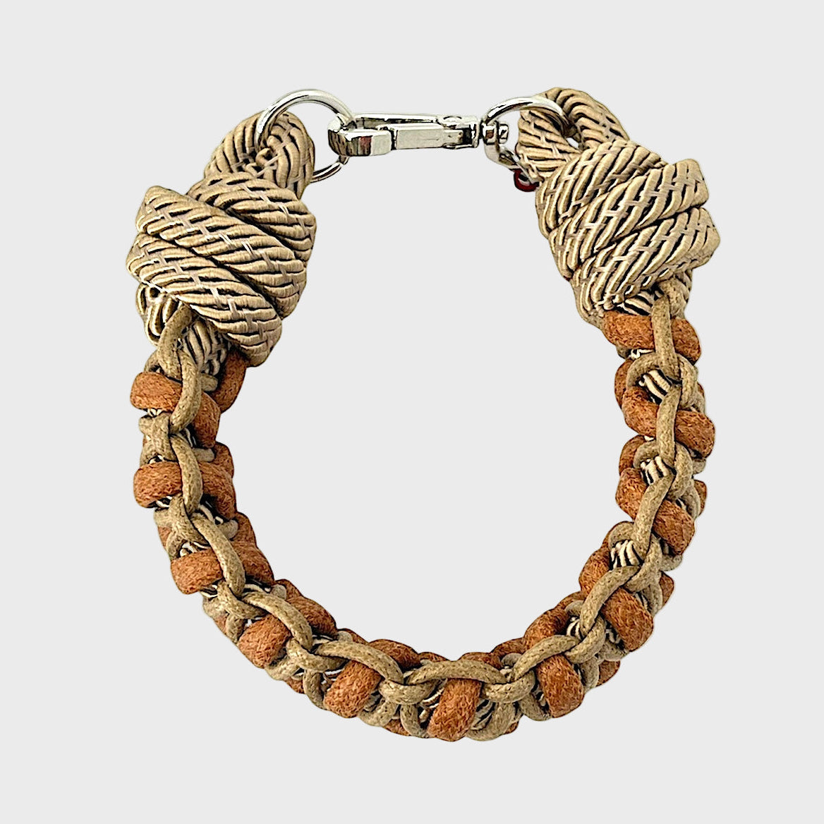 A photo taken from above of a braided macramé bracelet in shades of brown and light brown with a silver clasp.