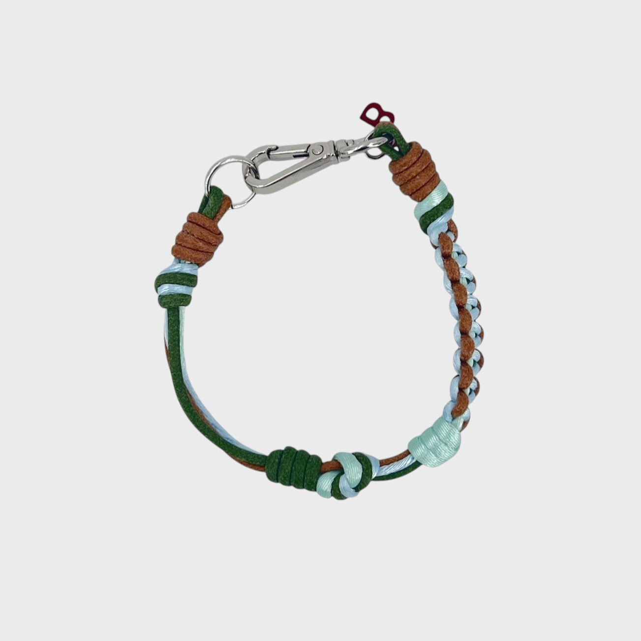 A photo taken from above of a thin braided macramé bracelet in shades of Green, blue and brown, with a silver clasp.