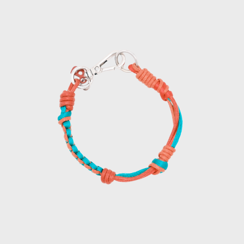 A photo taken from above of a thin braided macramé bracelet in shades of red and green, with a silver clasp.