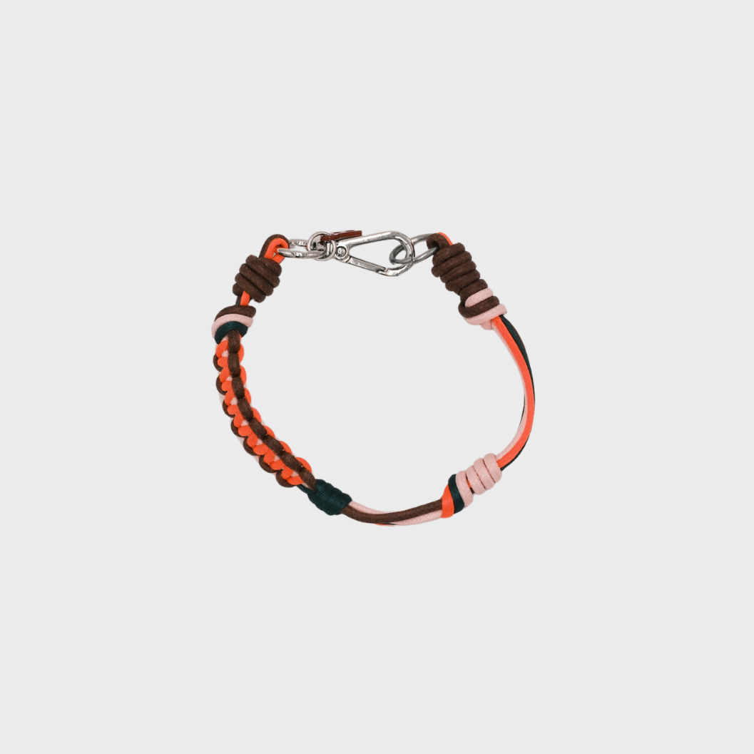 A photo taken from above of a thin braided macramé bracelet in shades of neon orang, brown and dark green, with a silver clasp.