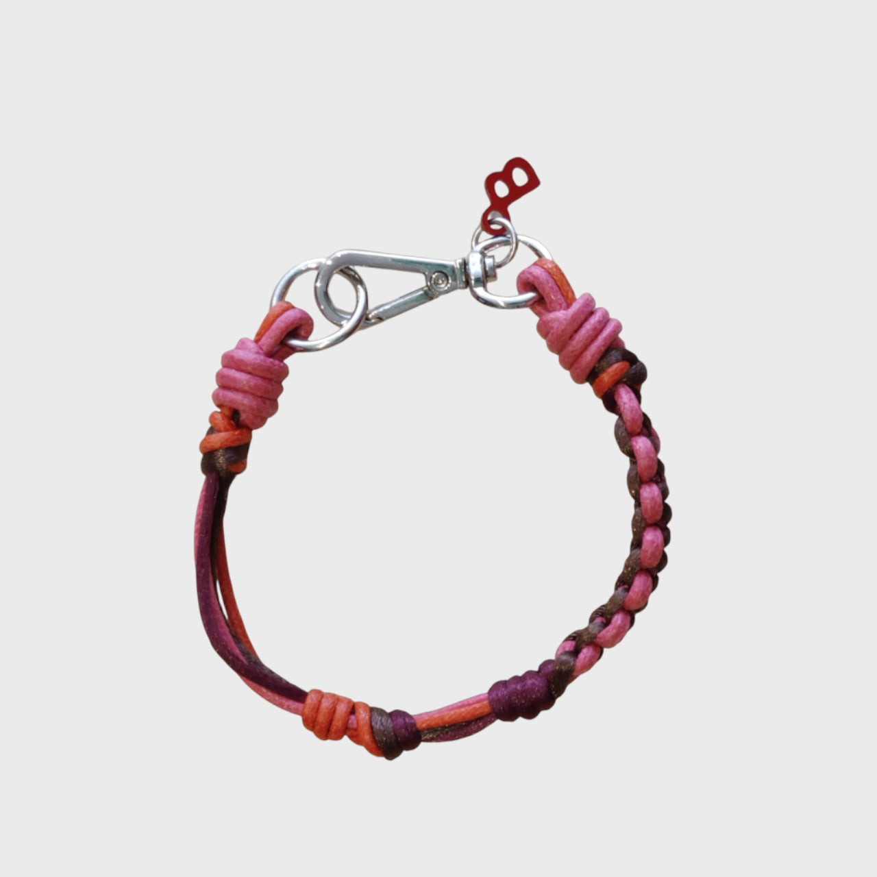 A thin braided bracelet with pink, red and brown macramé, featuring a silver metal clasp.