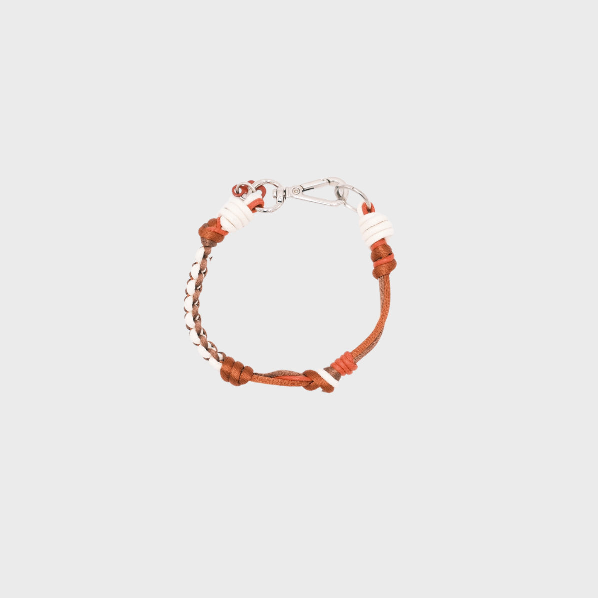 A photo taken from above of a thin braided macramé bracelet in shades of red, white and brown, with a silver clasp.