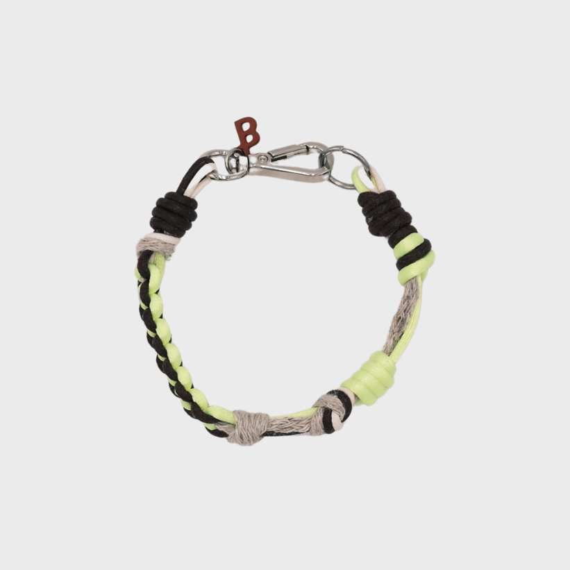 A photo taken from above of a thin braided macramé bracelet in shades of neon yellow, beige and brown, with a silver clasp.