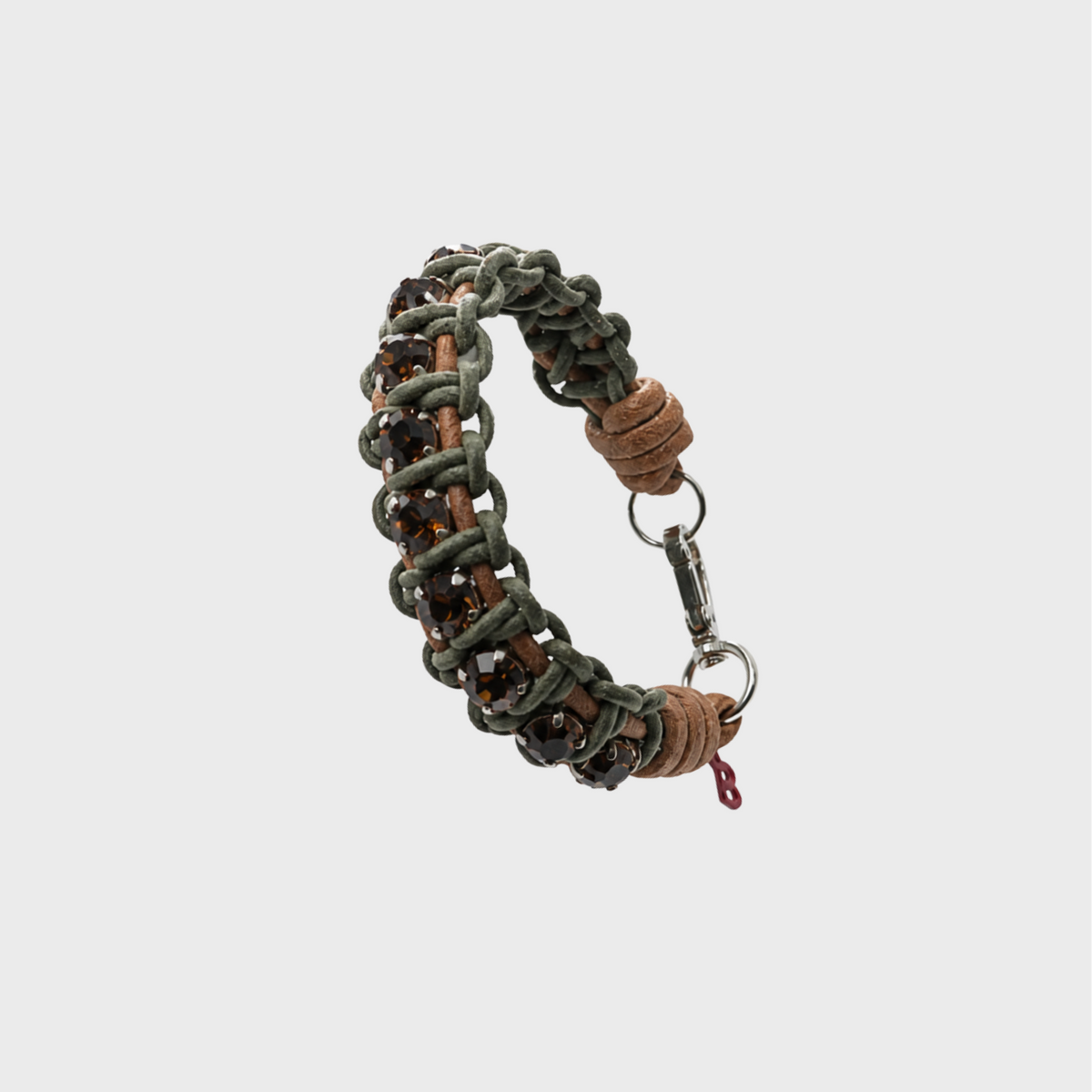 A handmade macrame bracelet featuring olive green cord, brown leather, and clear faceted crystals on a light gray background.