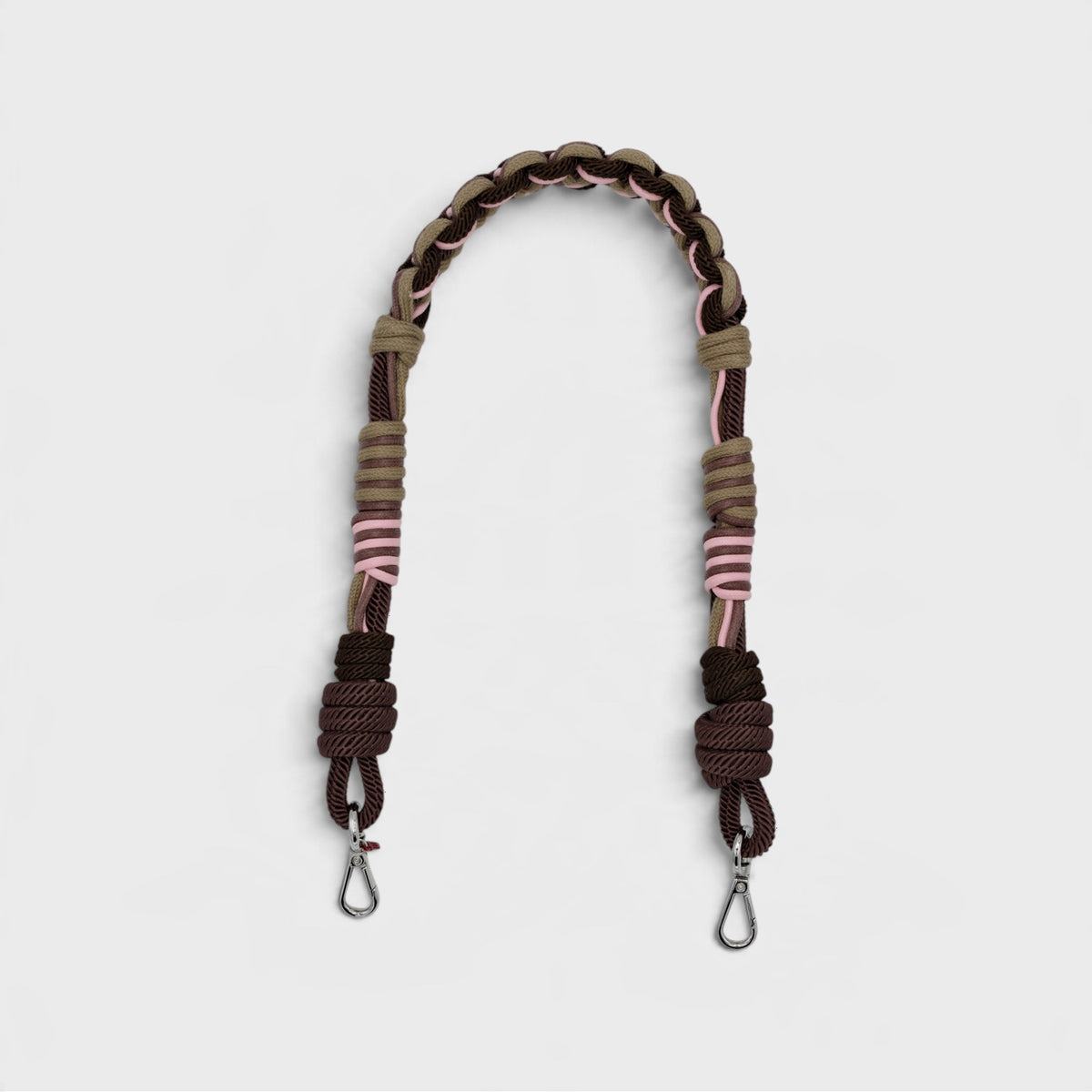 A braided and knotted macrame shoulder strap in brown, beige, and pink, with silver metal snap hooks at the ends, shown on a light gray background.