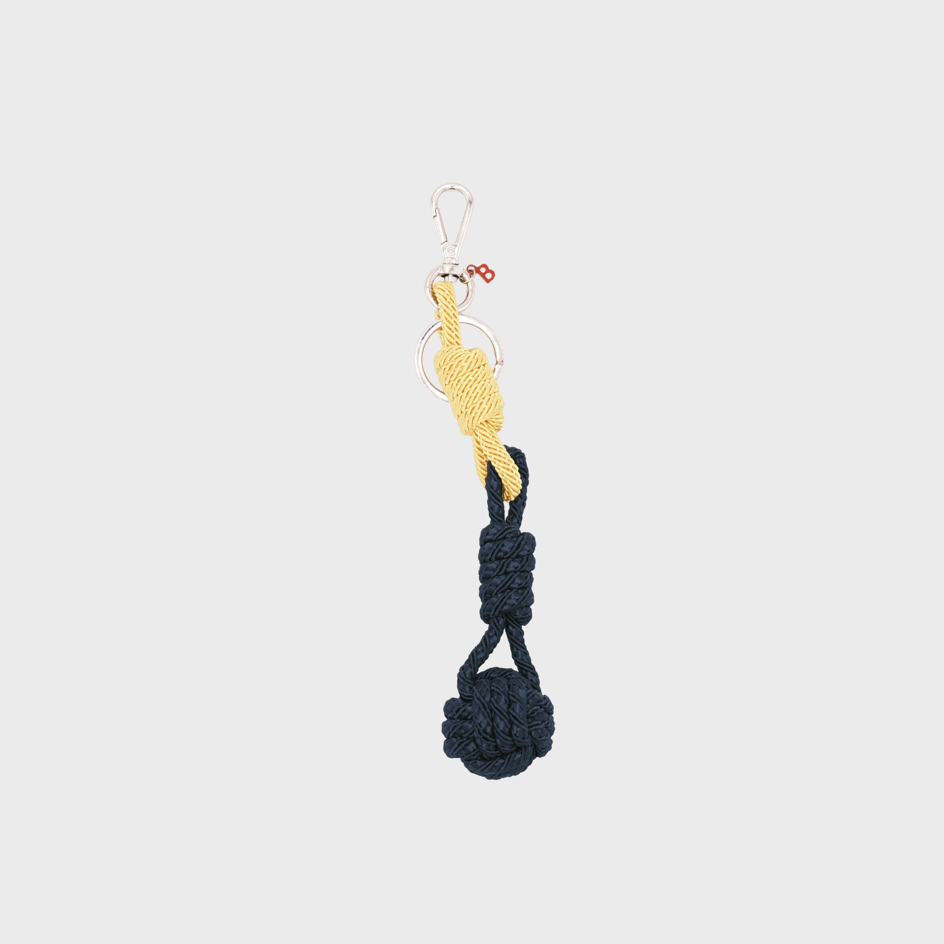 A macramé keychain representing a ball inspired by sailors knots. The straight upper part is bright yellow and the ball part is dark blue.
