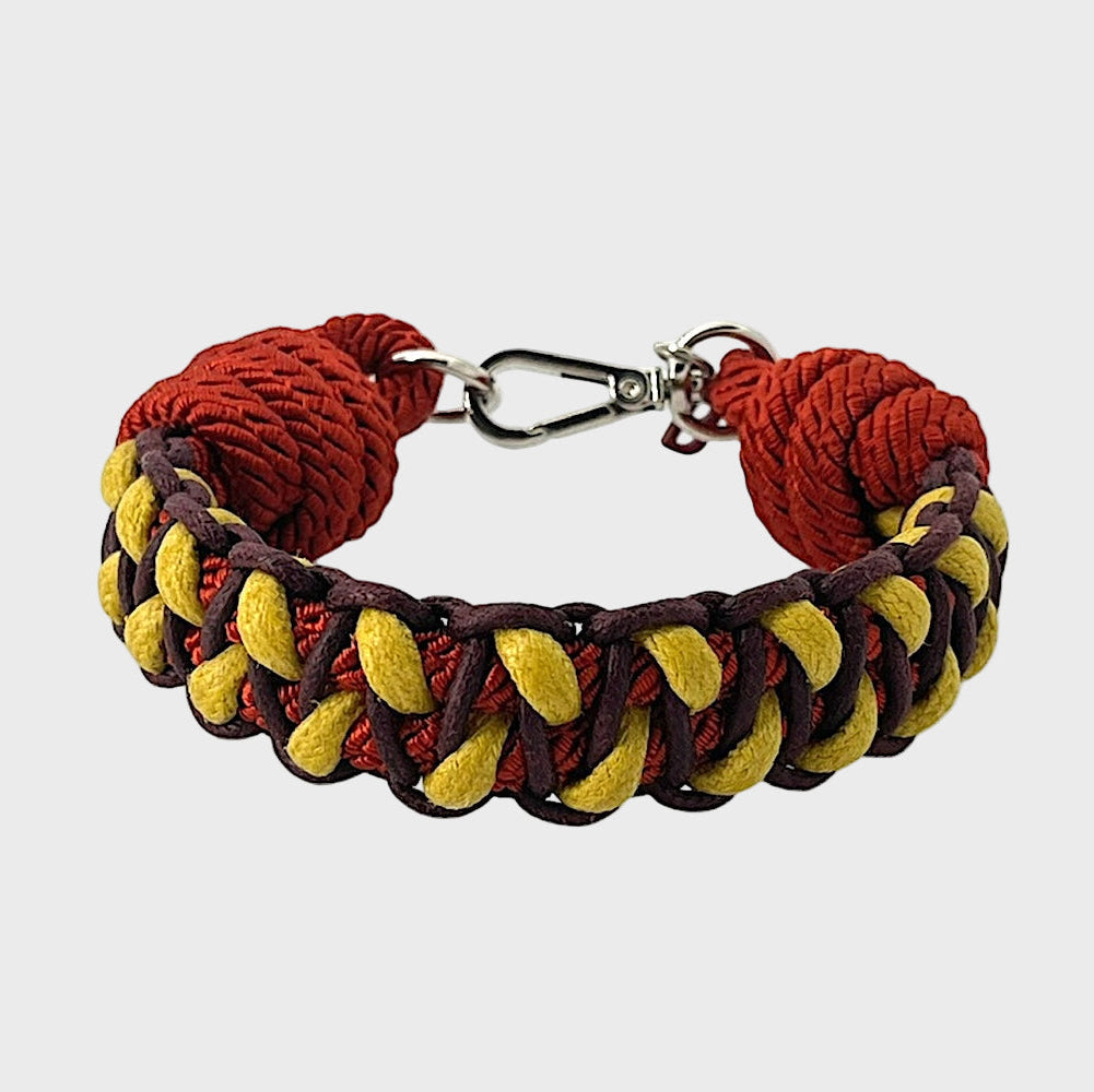 A braided macramé bracelet with shades of yellow, burgundy and red. It ends and a silver clasp, shown on a light gray background.