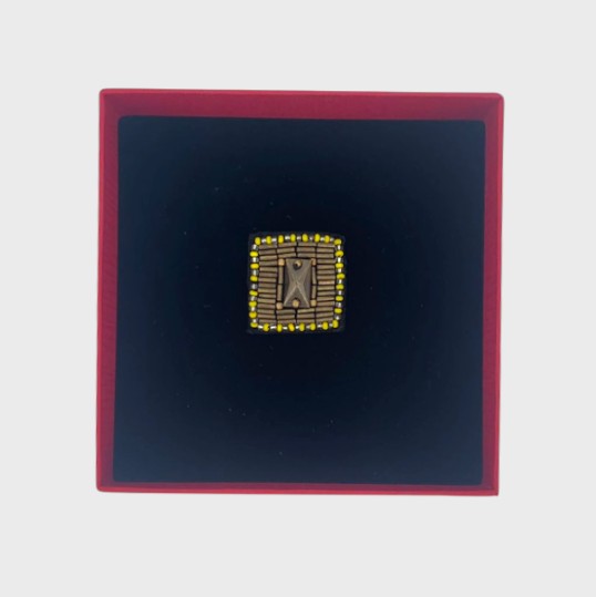 An embroidered brooch representing a golden button in a red box.