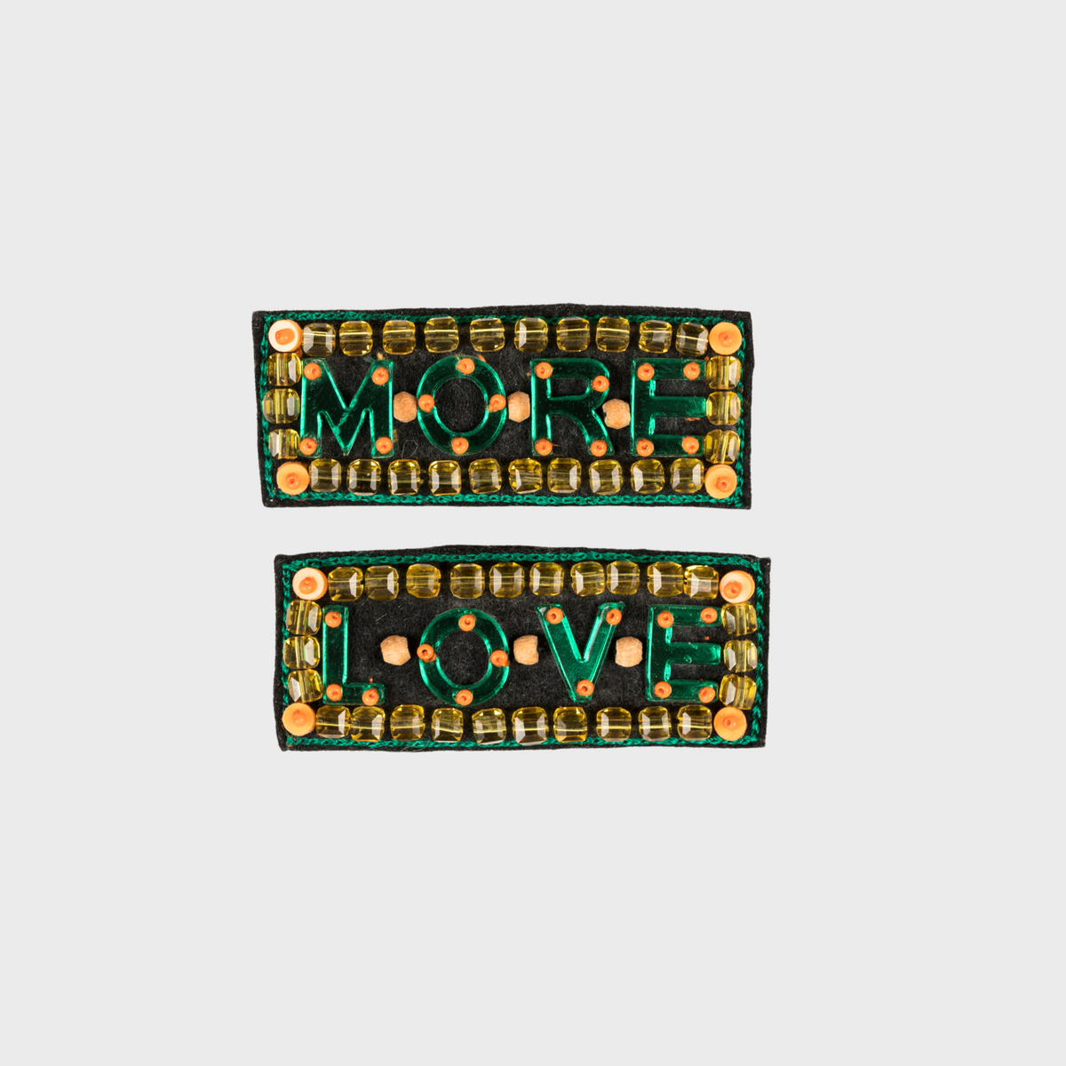 Two rectangular embroidered brooch with 'MORE LOVE' text on a light gray background
