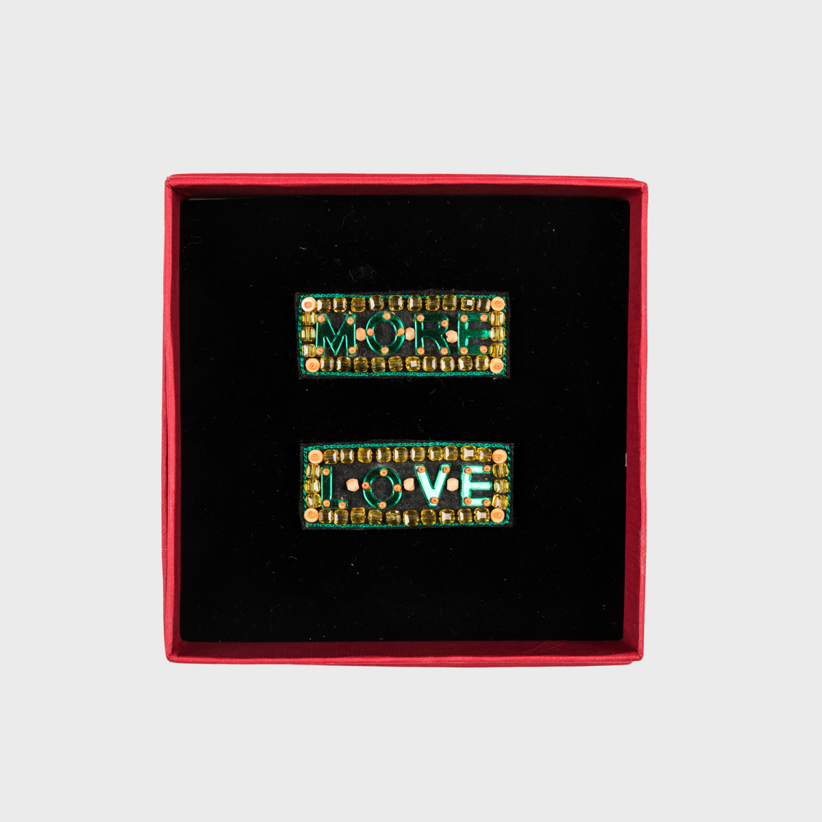 Two decorative brooches with 'MORE' and 'LOVE' text in a red box on a light gray background