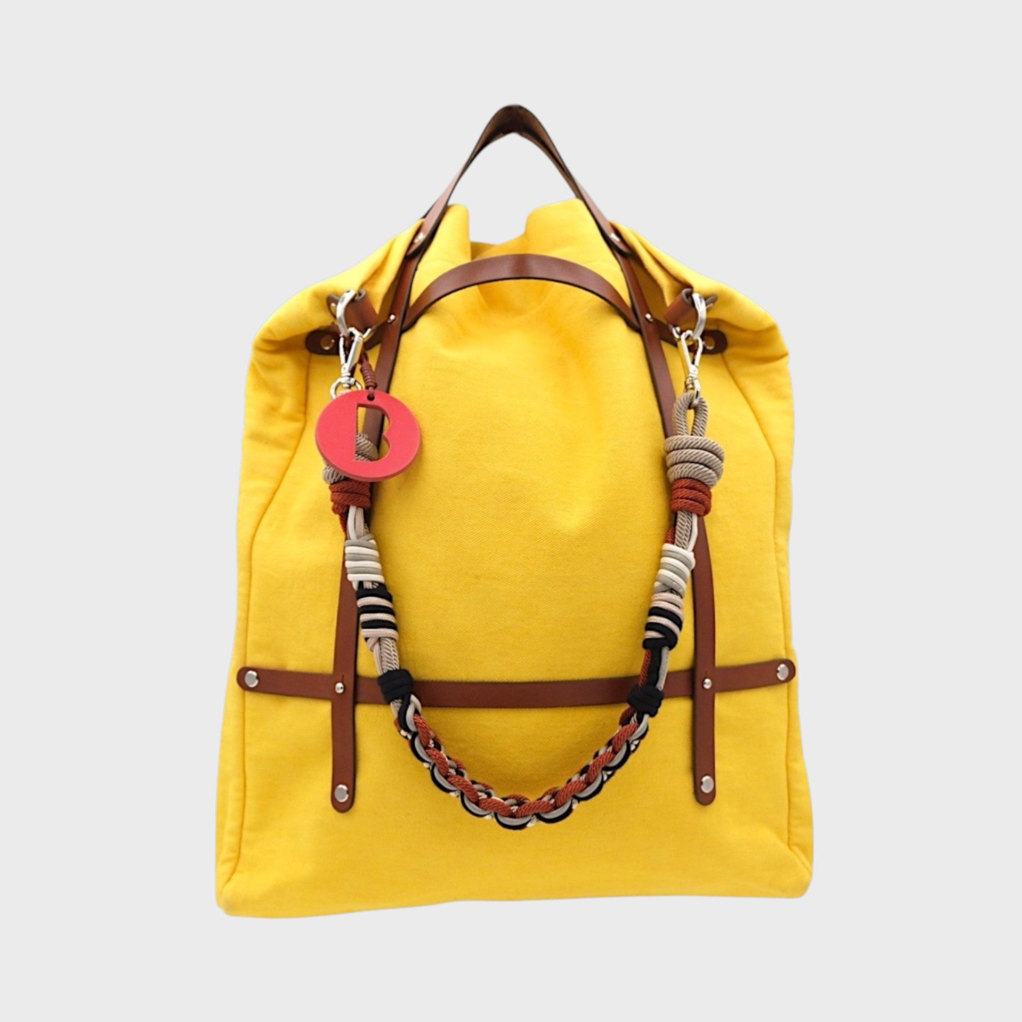 A canvas tote bag in a yellow color, featuring brown leather straps and a decorative beaded shoulder strap with black, brown and grey details.