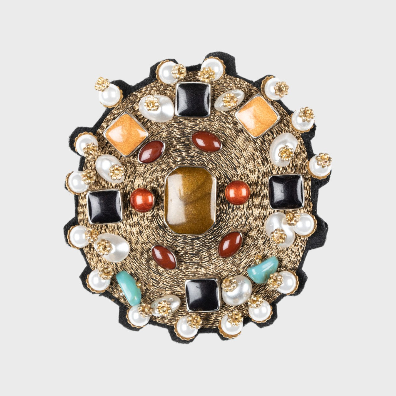 An embroidered brooch representing a golden yourte with several stones on it.