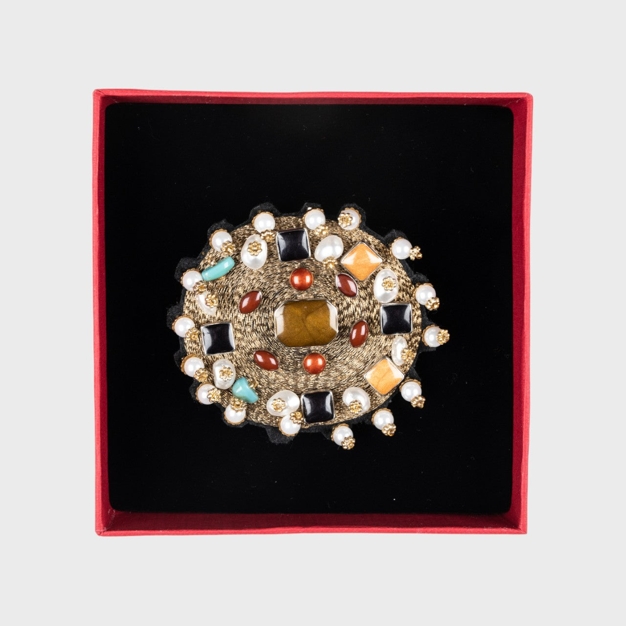 An embroidered brooch representing a golden yourte in a box.