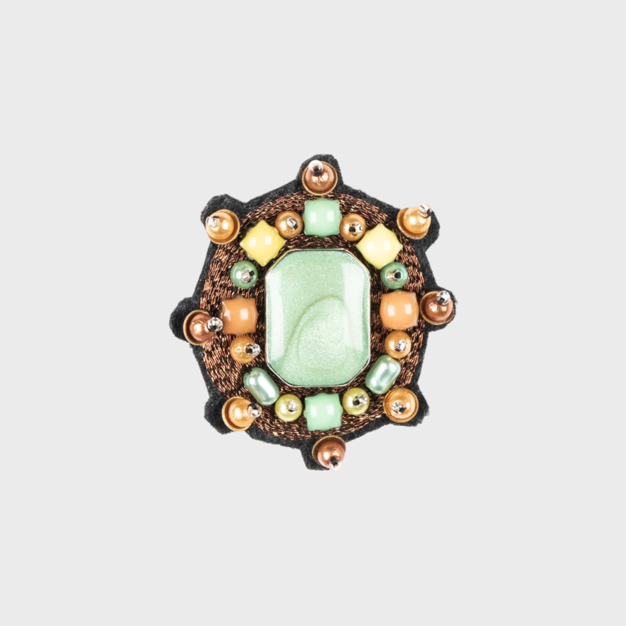 An embroidered brooch representing a small brown yourte with a green centered stone.