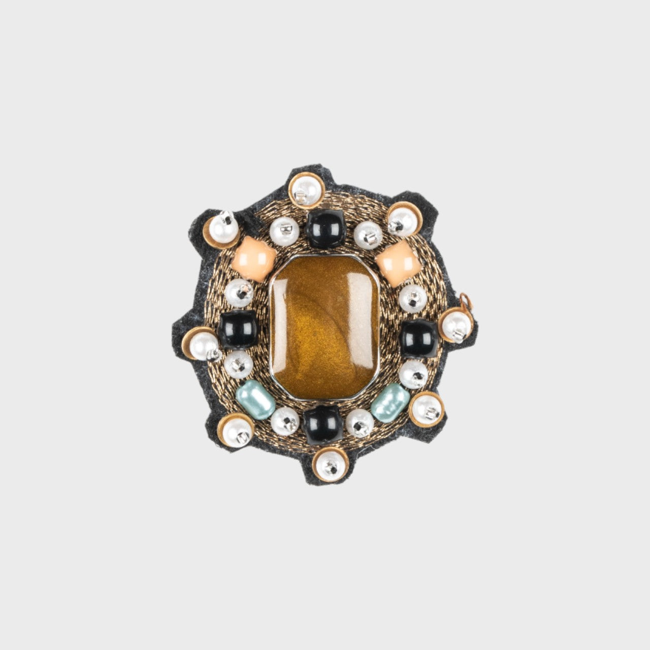 An embroidered brooch representing a mini yourte with a yellow stone in the center and golden details.
