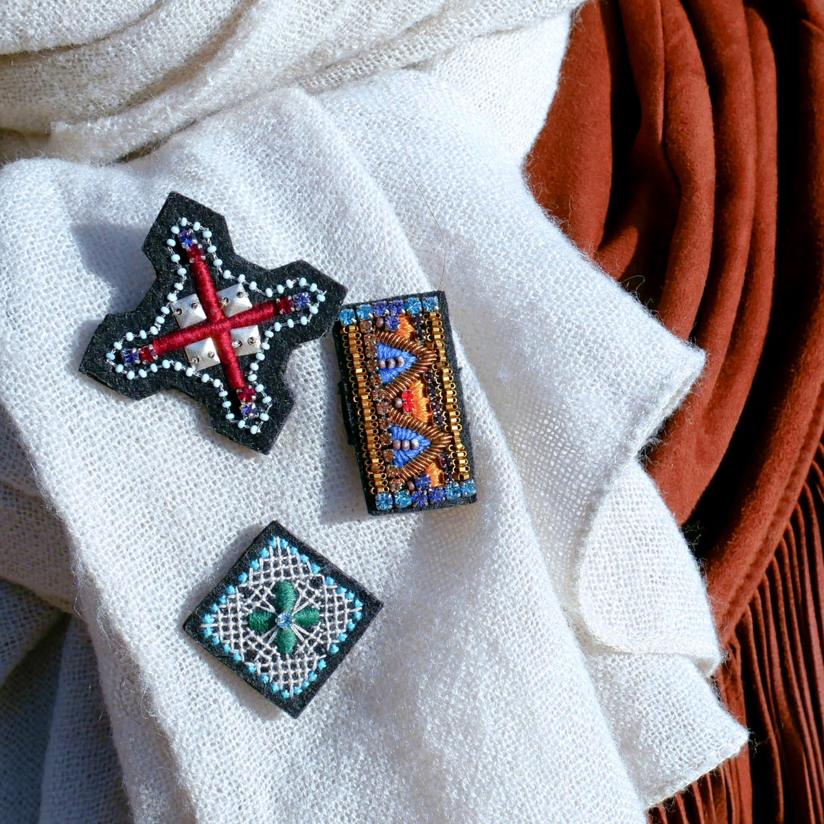 Three embroidered brooch on a white scarf.