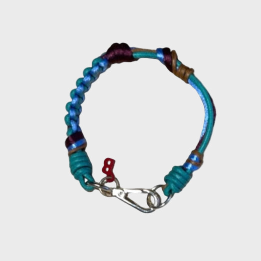 A photo taken from above of a thin braided macramé bracelet in shades of blue, green, purple and brown, with a silver clasp.