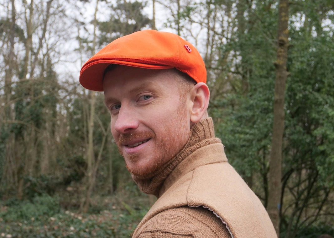 A man wearing an orange flat cap in cotton.
