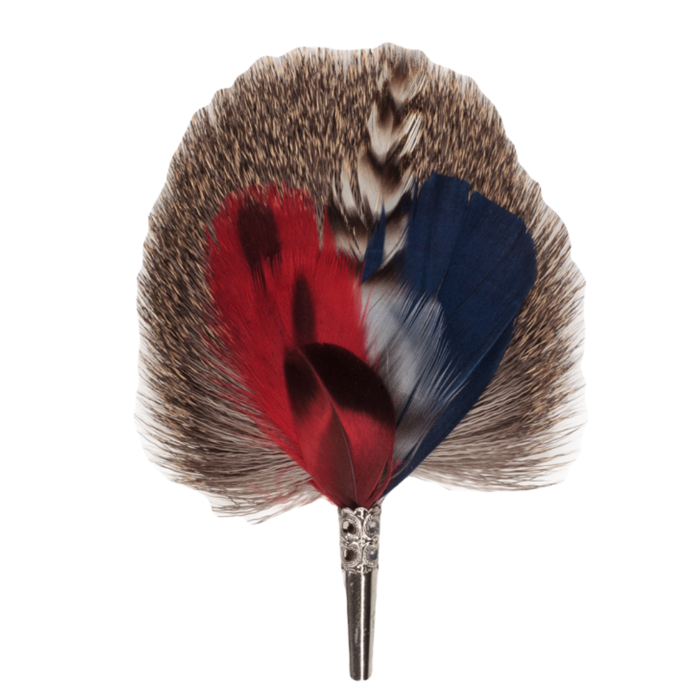 A brooch featuring a combination of red, blue, and brown dyed feathers, with a metallic clasp, handmade in Germany.