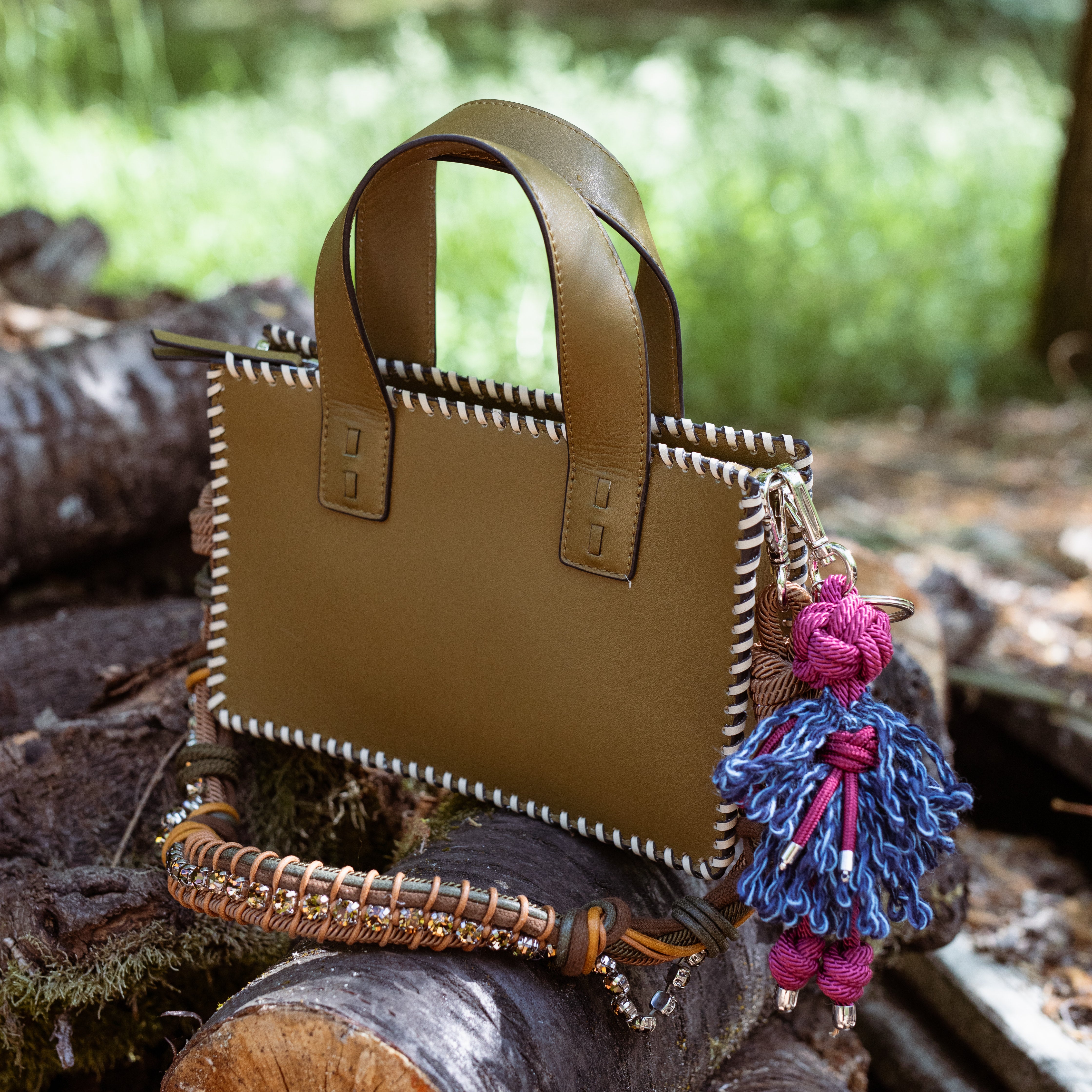 Multicolored braided macramé bag strap in dark green and brown, featuring some green colored beads and shown on sage coloured leather maori handbag in the forest.