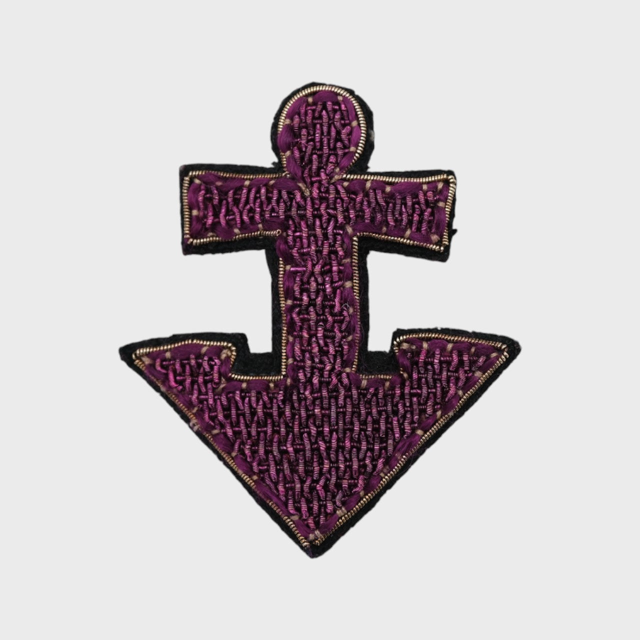 An embroidered brooch representing a purple anchor with golden details. 
