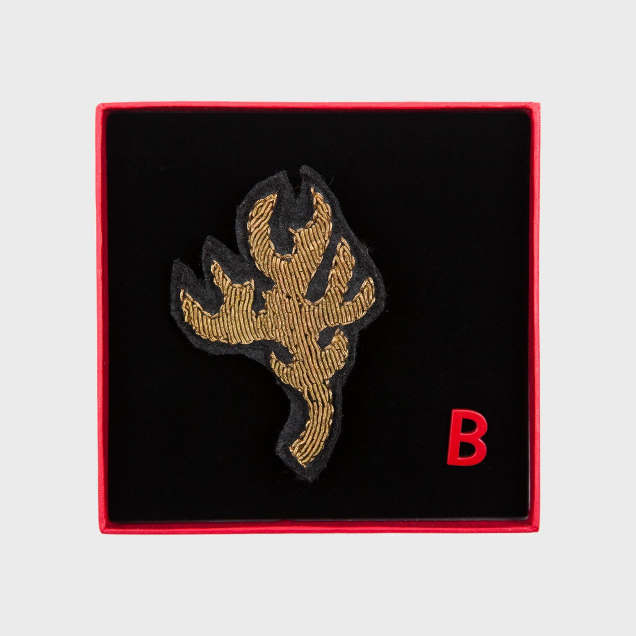 An embroidered brooch representing a golden antler in a box. 