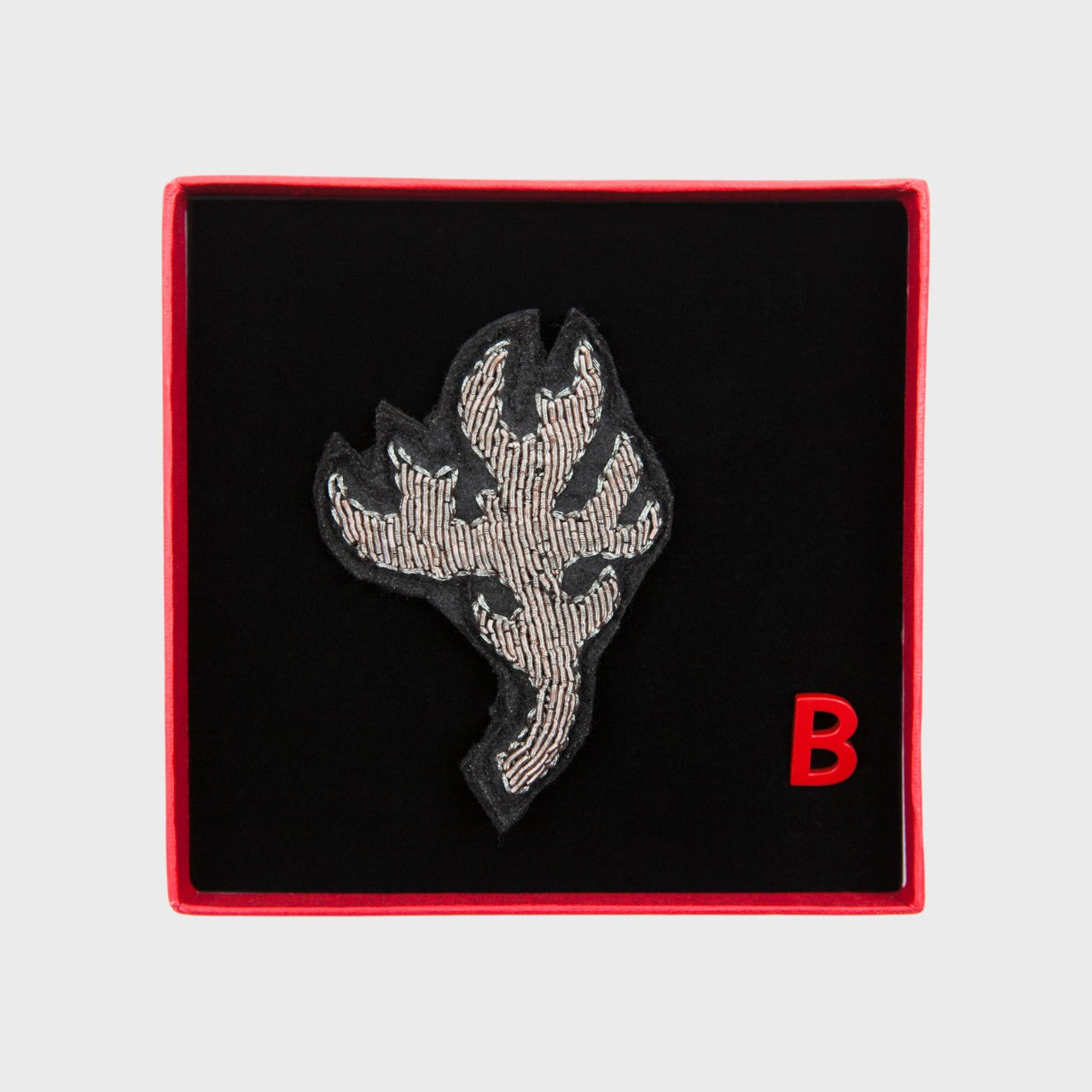 An embroidered brooch representing a silver antler in a box. 