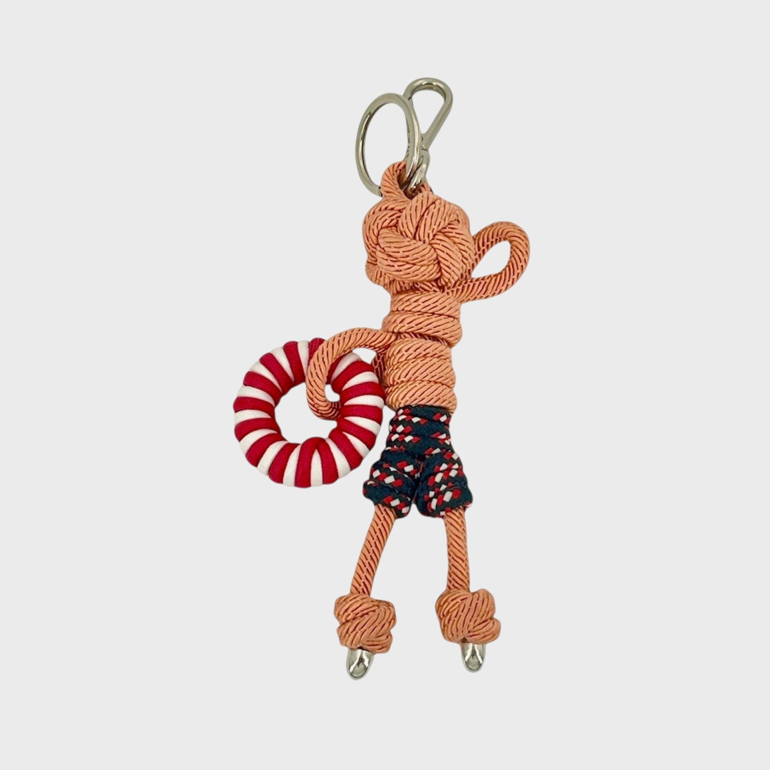 Handmade tan macramé bag charm featuring a male character, meant to be at the beach, wearing blue and red swimming shorts and holding a pool float. He is attached to a silver clasp.