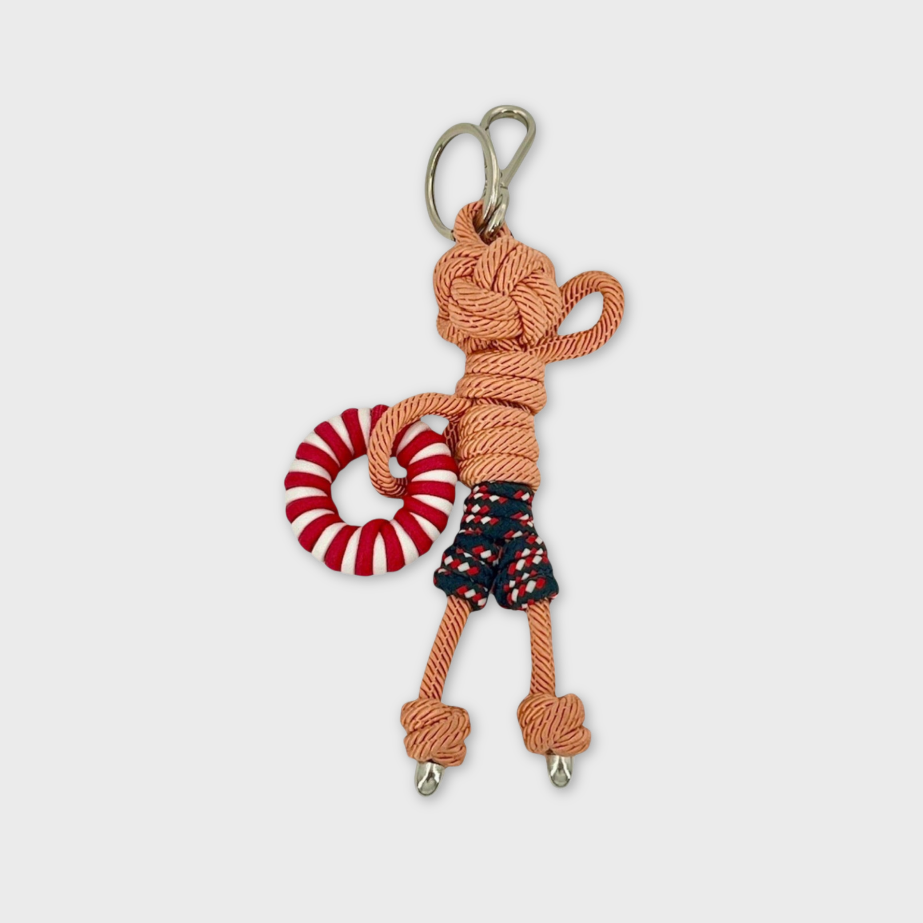 Handmade tan macramé bag charm featuring a male character, meant to be at the beach, wearing blue and red swimming shorts and holding a pool float. He is attached to a silver clasp.