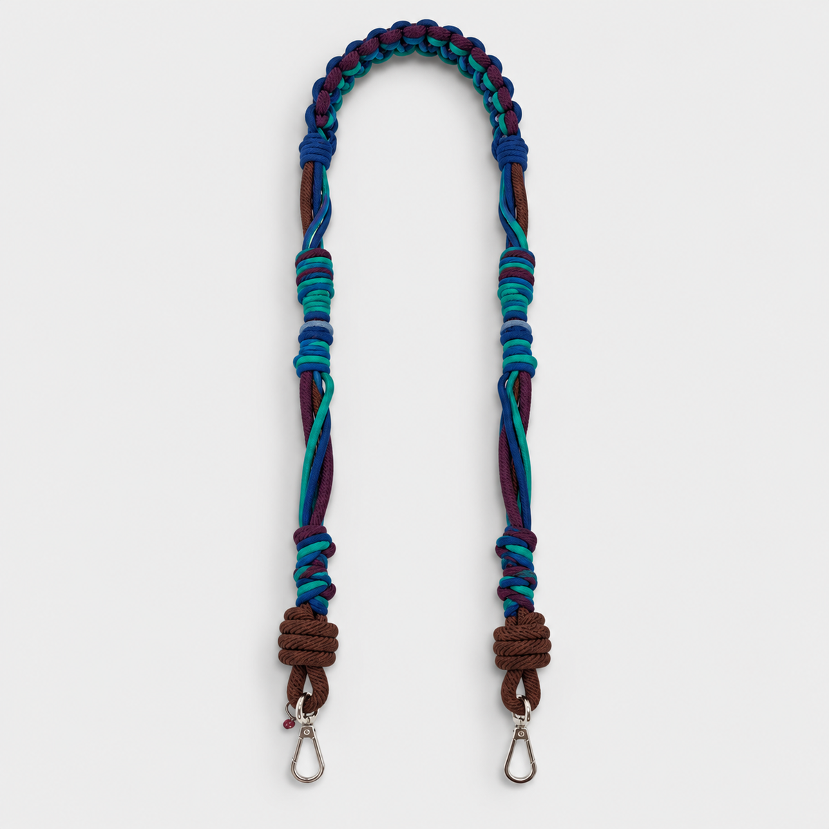 Multicolored braided macramé bag strap in various blues, with accents of purple and brown shown on a light gray background.