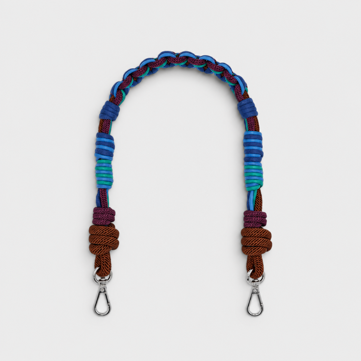 Multicolored braided macramé bag strap in various blues, with accents of purple and brown shown on a light gray background.
