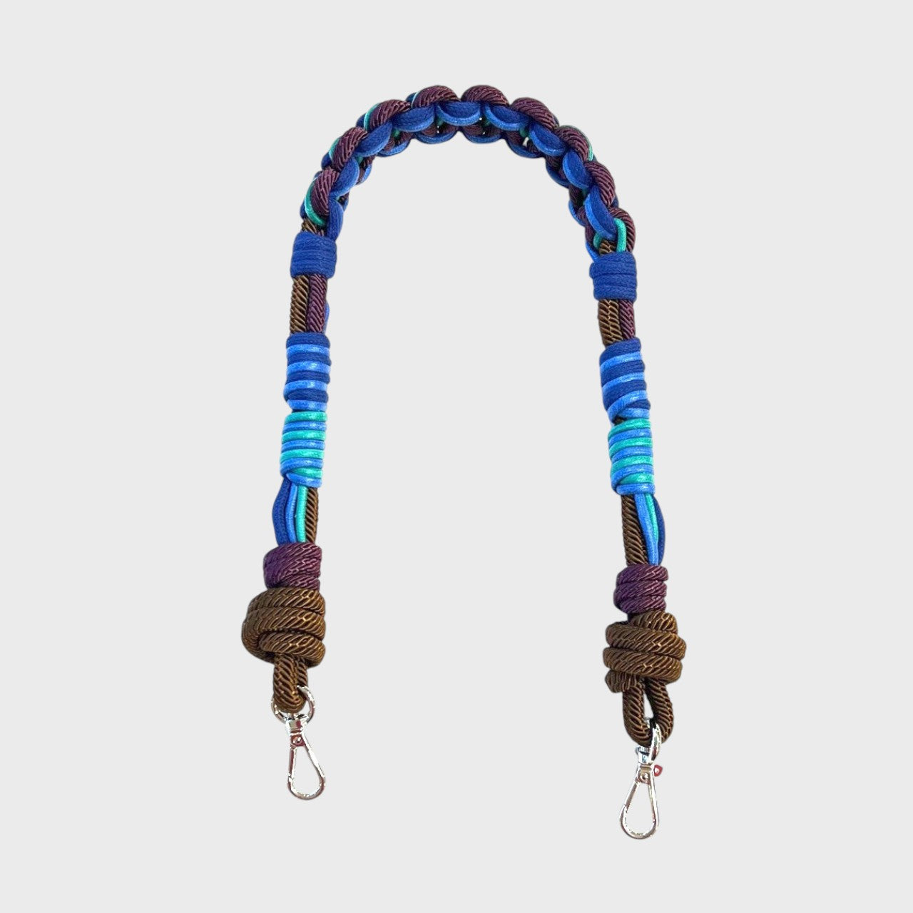Multicolored braided macramé bag strap in various blues, with accents of purple and brown shown on a light gray background.