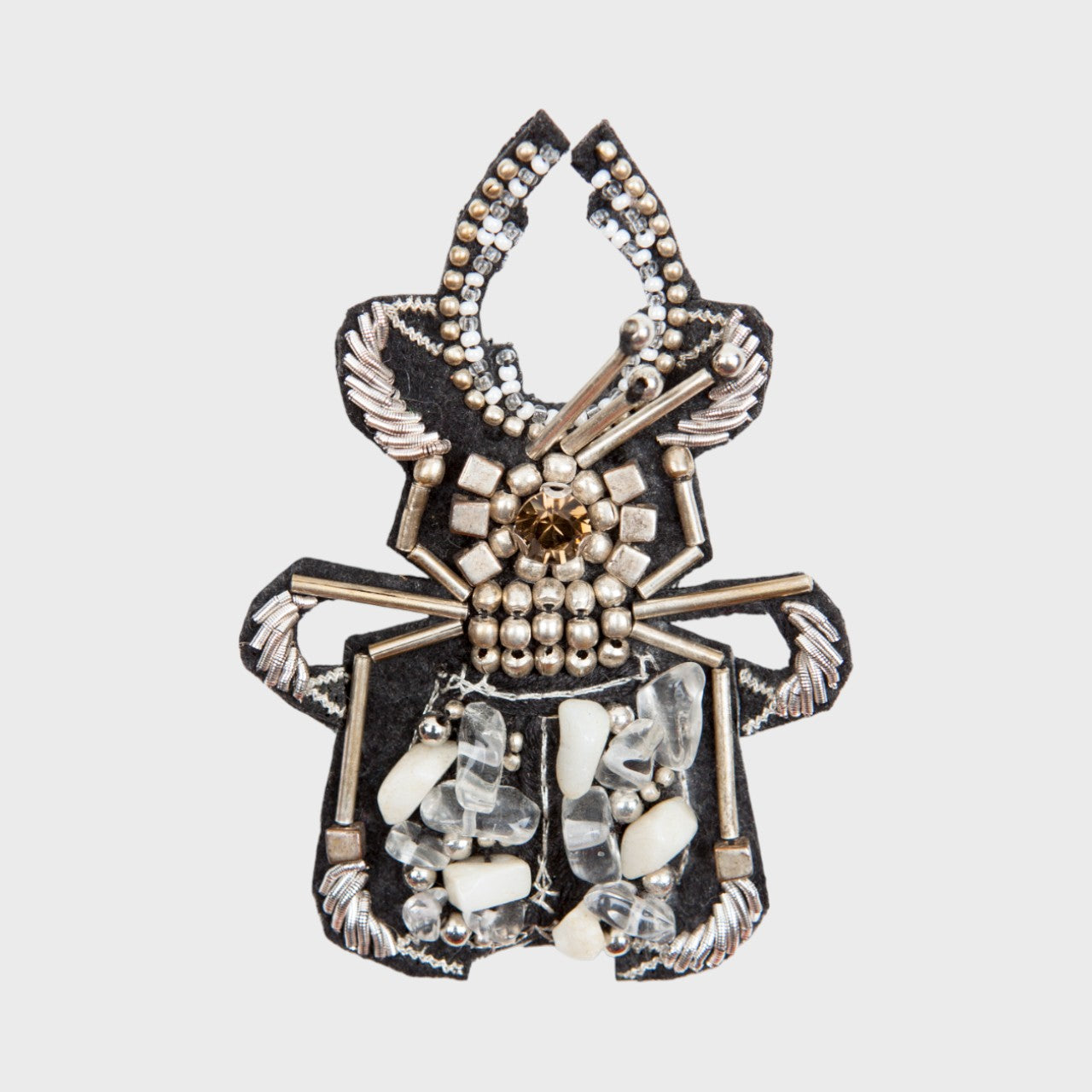 An embroidered brooch representing a beetle with silver and white details. 