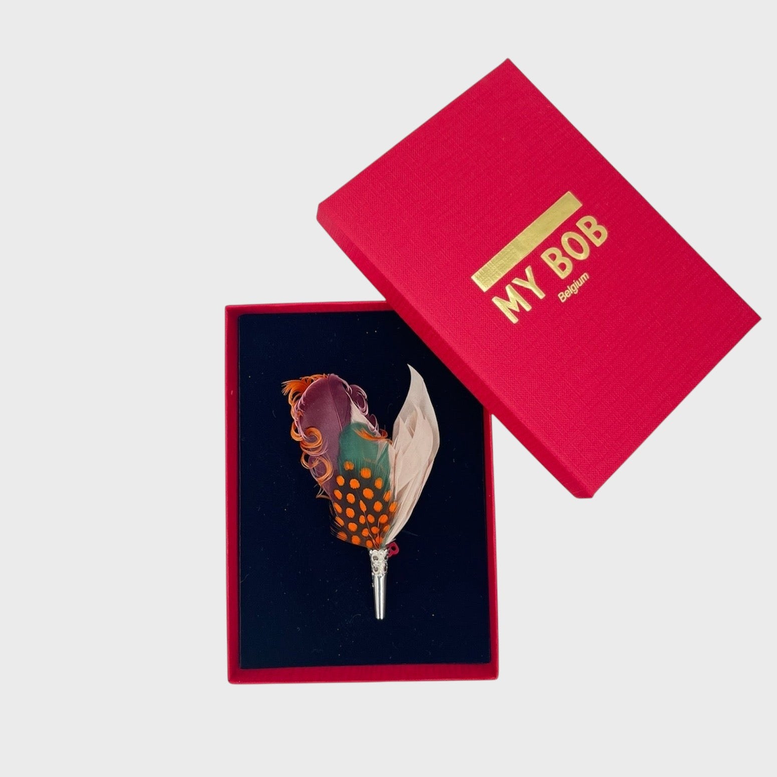 Burgundy, orange, green and beige feather brooch in a box on a light gray background