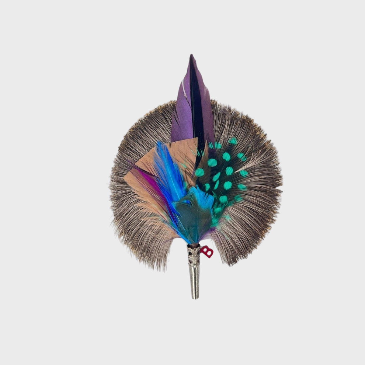 A feather brooch with purple, beige, green, blue and grey feathers and a silver metal clasp. 