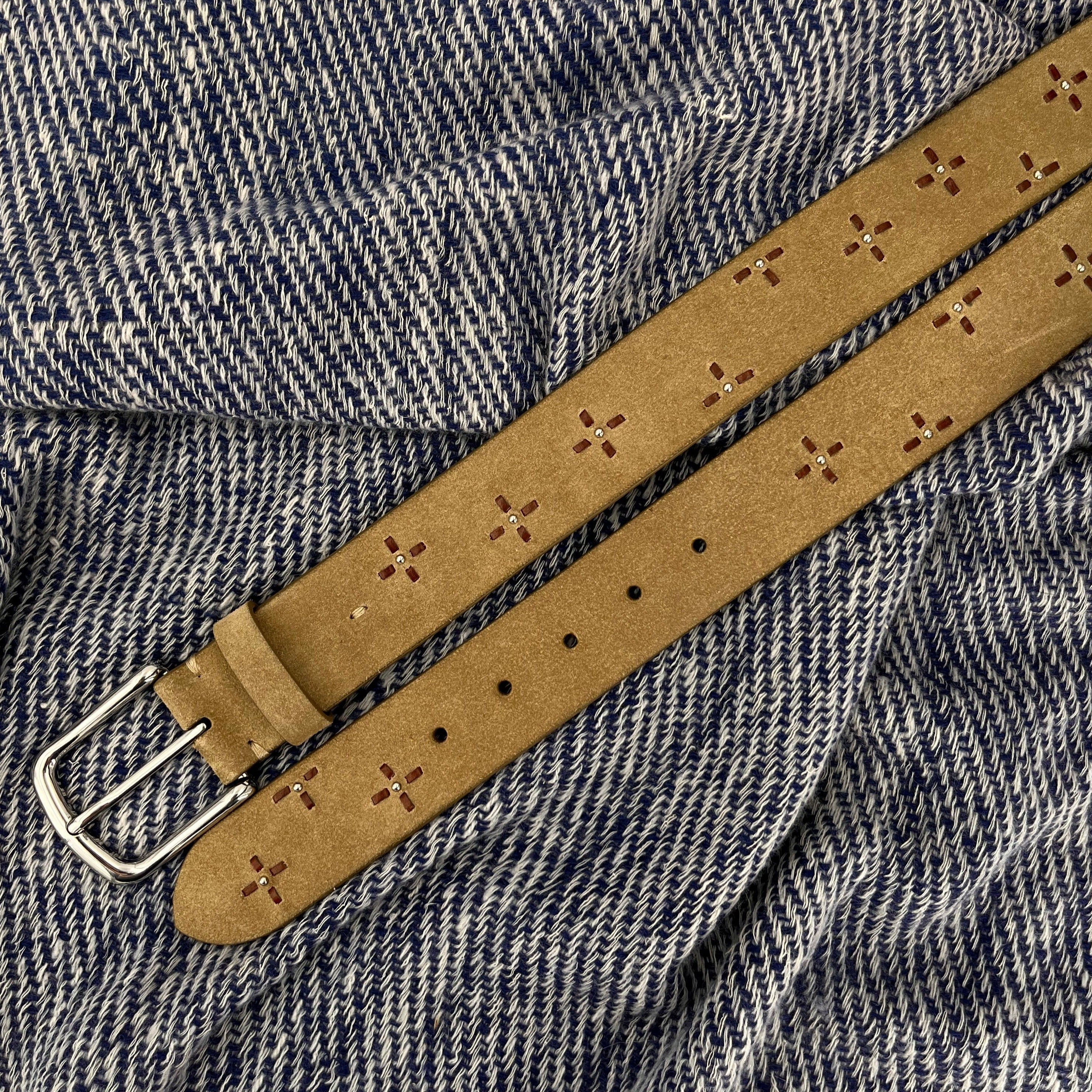 Beige suede belt with decorative flowers and a silver buckle on a white and blue bed cover.