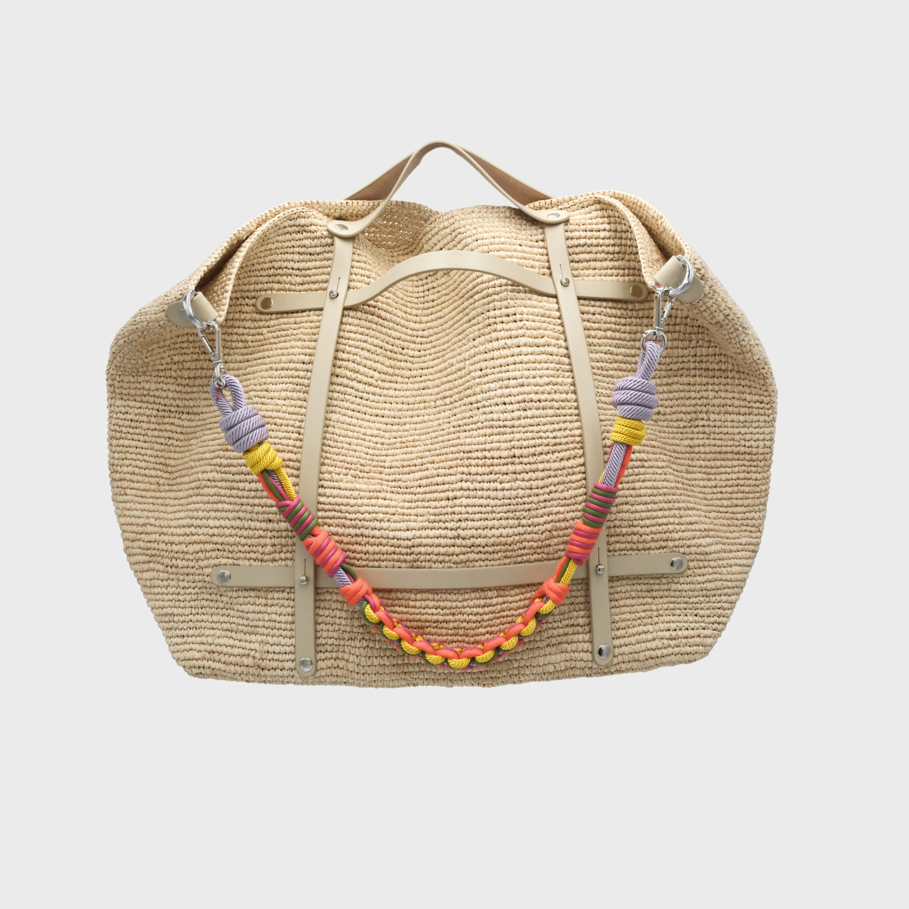 A natural woven straw weekender bag with beige leather straps and a colorful macramé rope shoulder strap with purple, yellow, and orange.