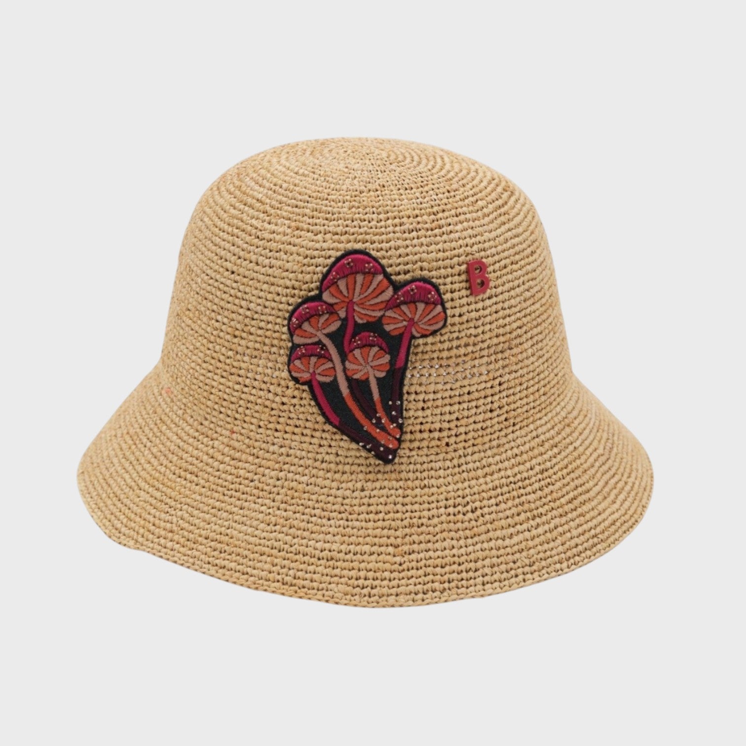 Beige raffia bucket hat with a myco mushrooms bucket brooch on a light gray background