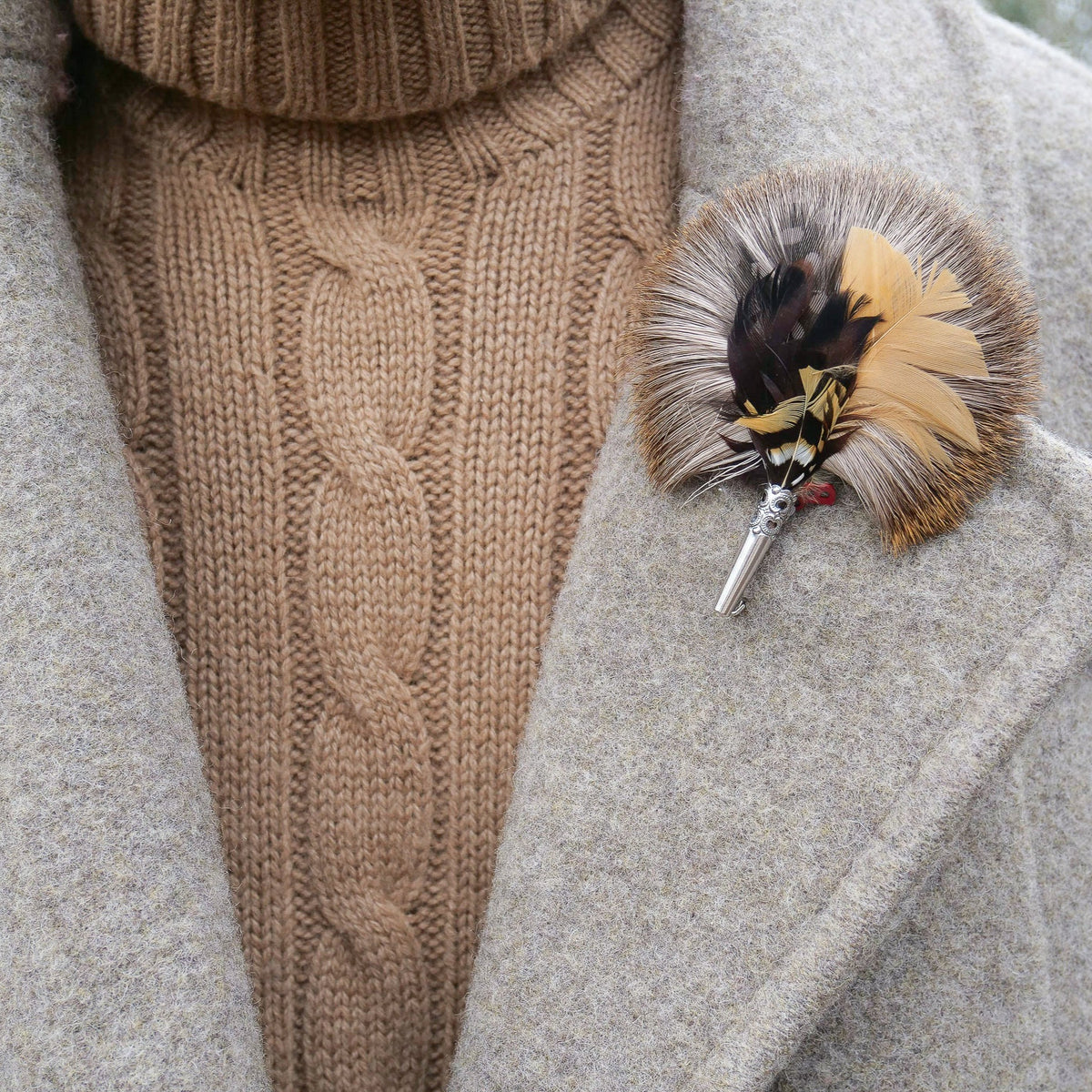 A close-up of a brown feather brooch, attached to a pin and affixed to a jacket.