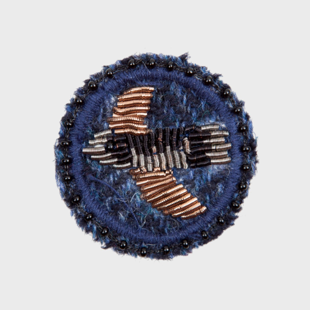 An embroidered brooch representing a gold and black bird in the middle of a blue circle. 