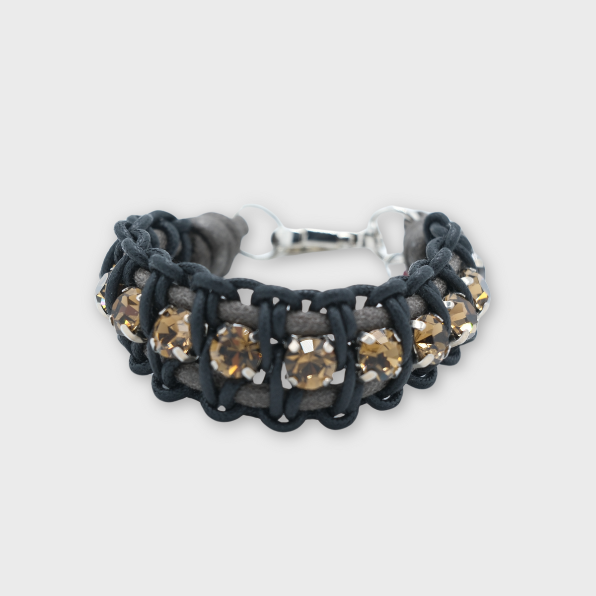 A black woven cord bracelet featuring a row of round, faceted champagne-colored crystals in silver settings, with a silver clasp closure, shown on a light gray background.