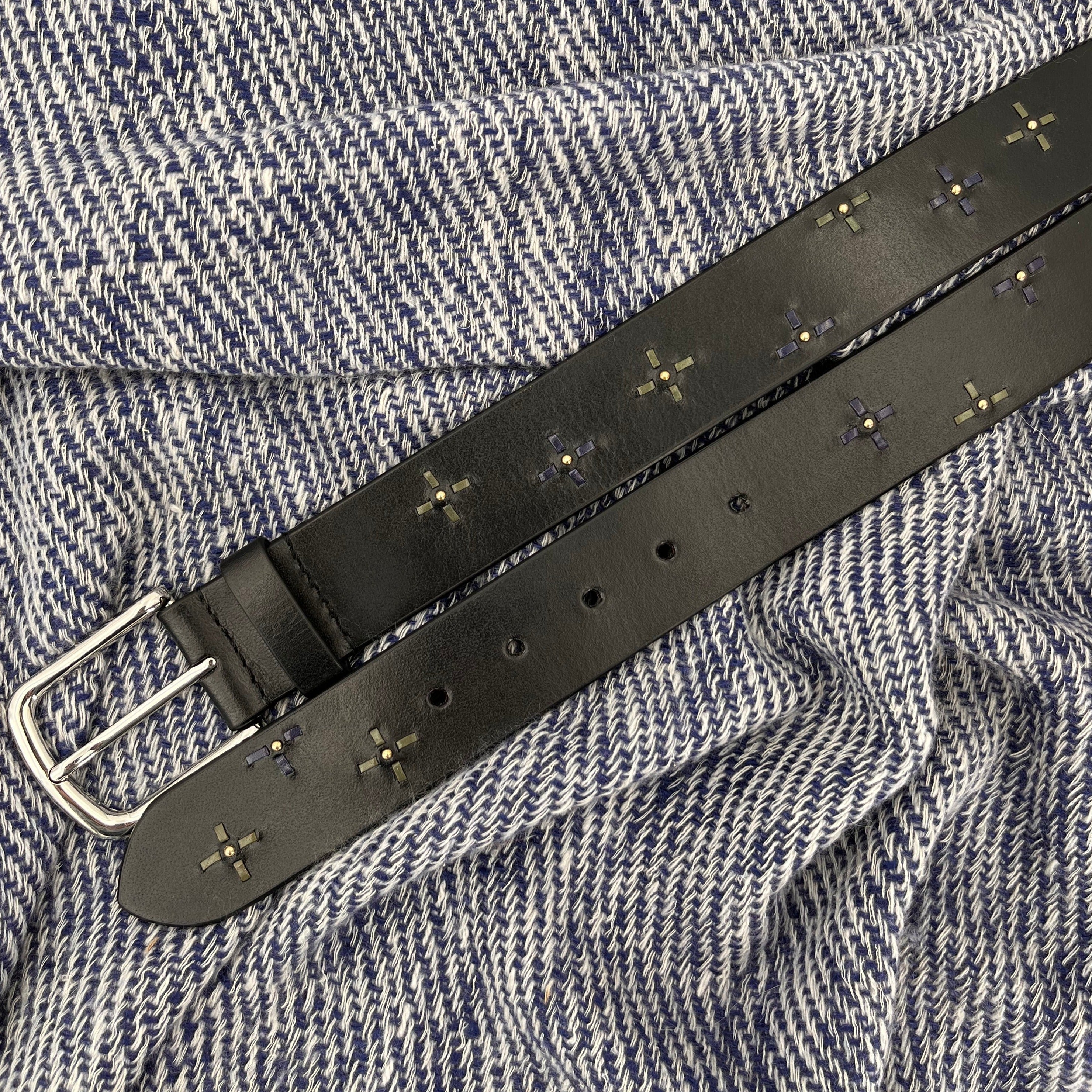 Black leather belt with floral embroidery and silver buckle on a white and blue bed cover.