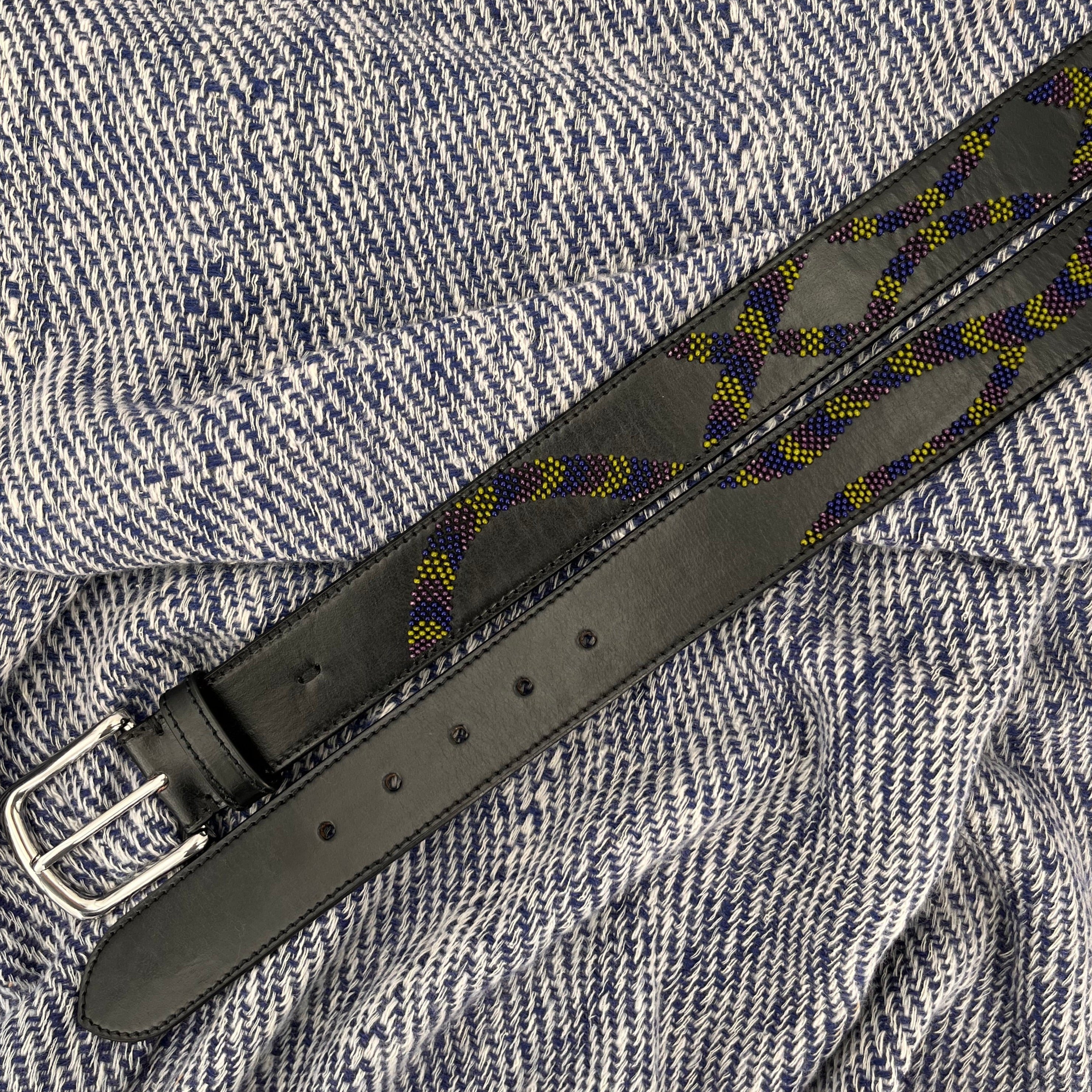 Black leather belt with a decorative snake embroidery and silver buckle on a blue and white bed cover.
