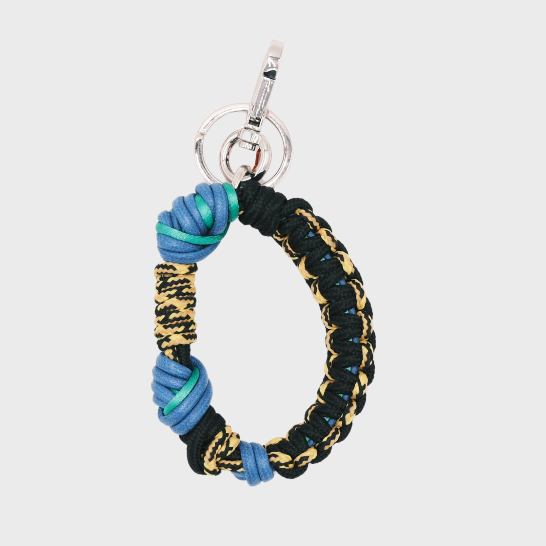 A woven macramé key chain with black, yellow, blue and green patterns, inspired by celtic knots, finished with silver-tone metal hardware.